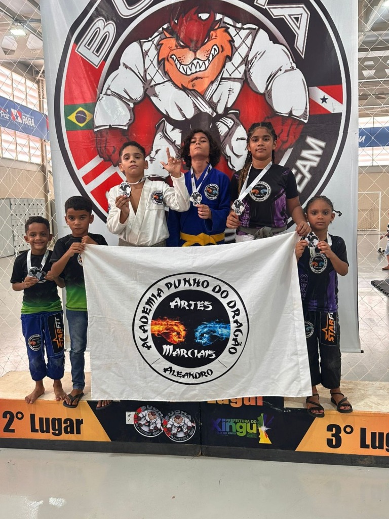 Alunos no pódio de competição segurando a bandeira da Academia Punho do Dragão