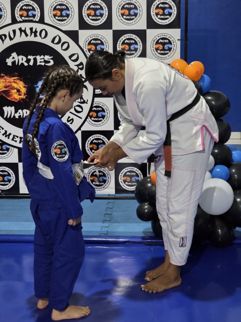 Momento de graduação com instrutora amarrando a nova faixa na aluna