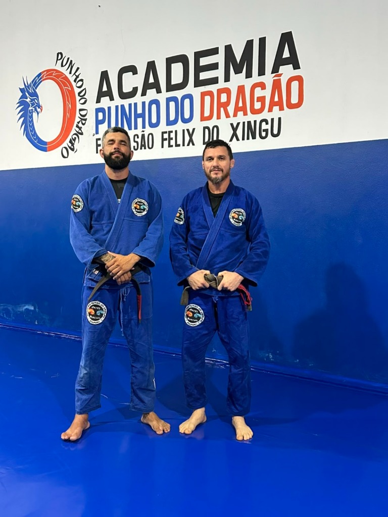 Professores de kimono azul em frente ao logotipo oficial da academia