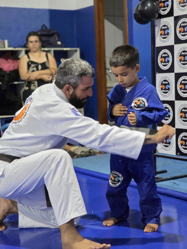 Professor faixa preta acompanhando e ajustando a faixa de aluno da turma Punho Kids no tatame
