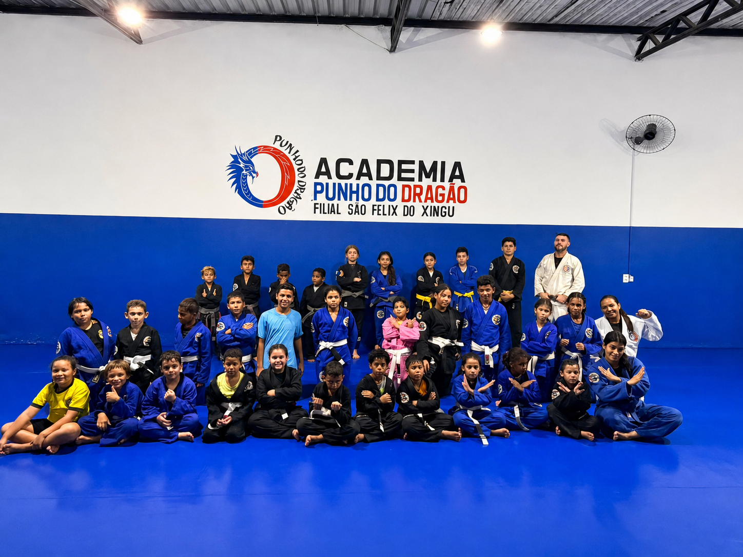 Turma Kids da Academia Punho do Dragão reunida no tatame, com a identidade da academia na parede ao fundo